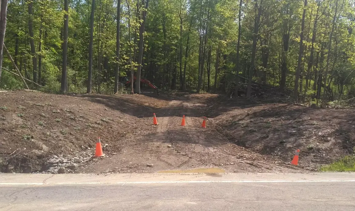 Landmark Enterprises excavation crew cutting a new gravel driveway off the road with safety cones in Dewittville, NY